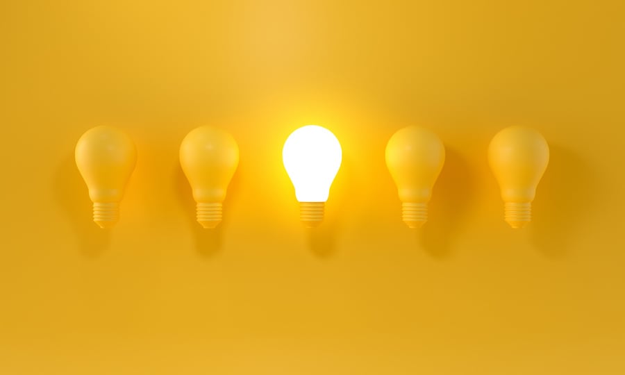 Glowing Light Bulb between the others on yellow light backgr